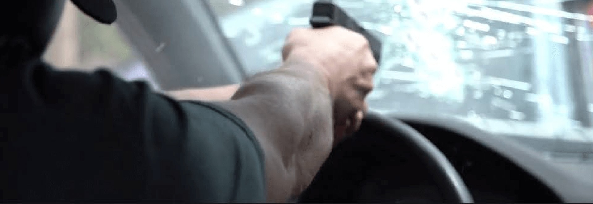 a man trying to break the windshield with a gun