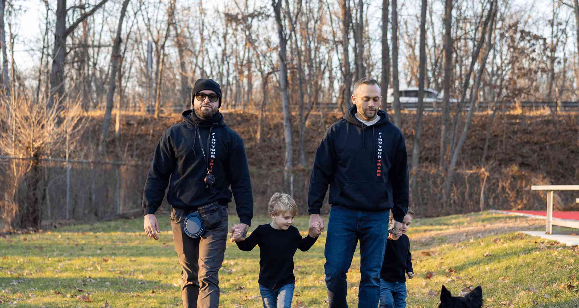 Father and son leisurely walking in the park with a dog on a sunny day.